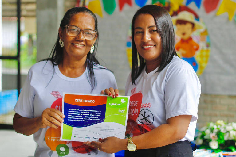 Duas mulheres sorriem e seguram um certificado em suas mãos