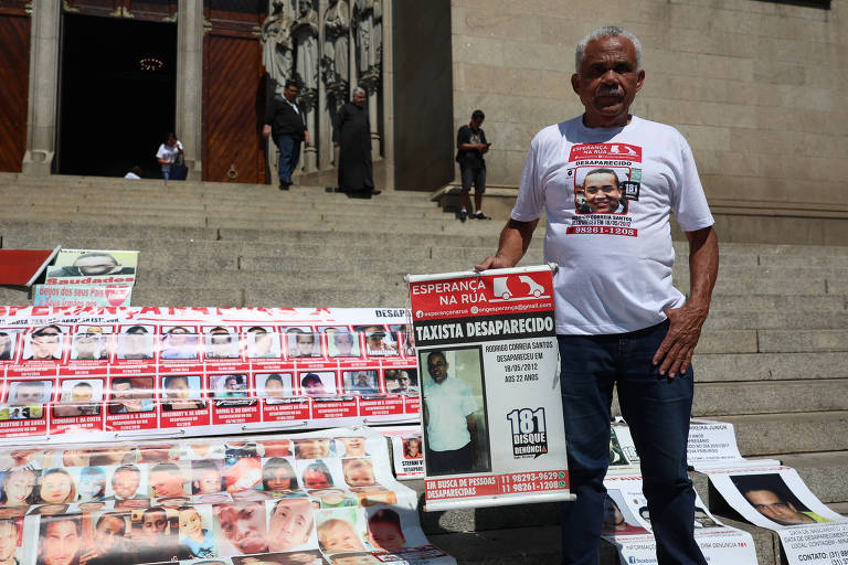 Homem em frente as escadarias da Sé segura um cartaz de desaparecido