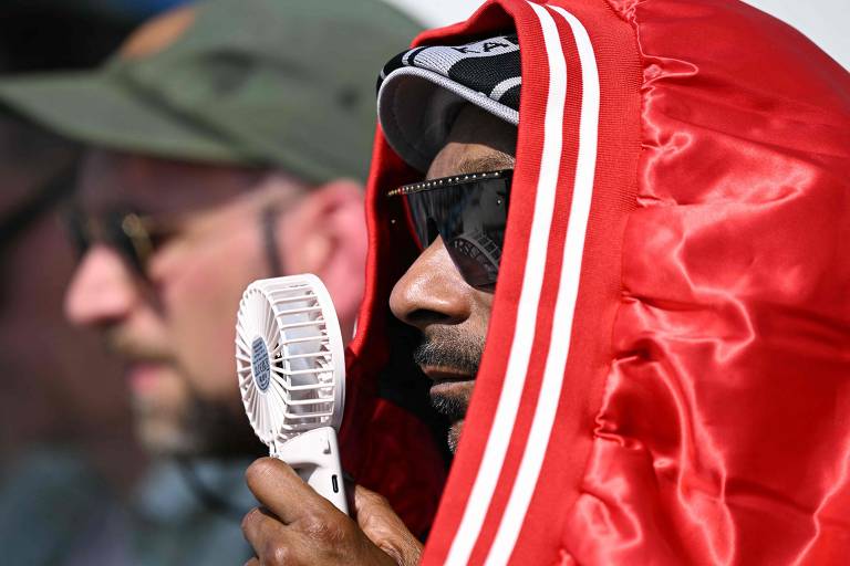 O rapper Snoop Dogg usa ventilador e casaco em cima da cabeça para se proteger do calor enquanto assiste à final masculina do skate nas Olimpíadas, em Paris