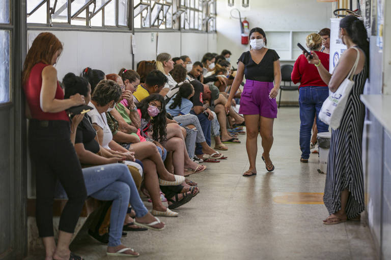 Usuários e usuários do SUS sentados à esquerda da imagem aguardando atendimento em um corredor de uma unidade básica de saúde de Ceilândia， no Distrito Federal. 