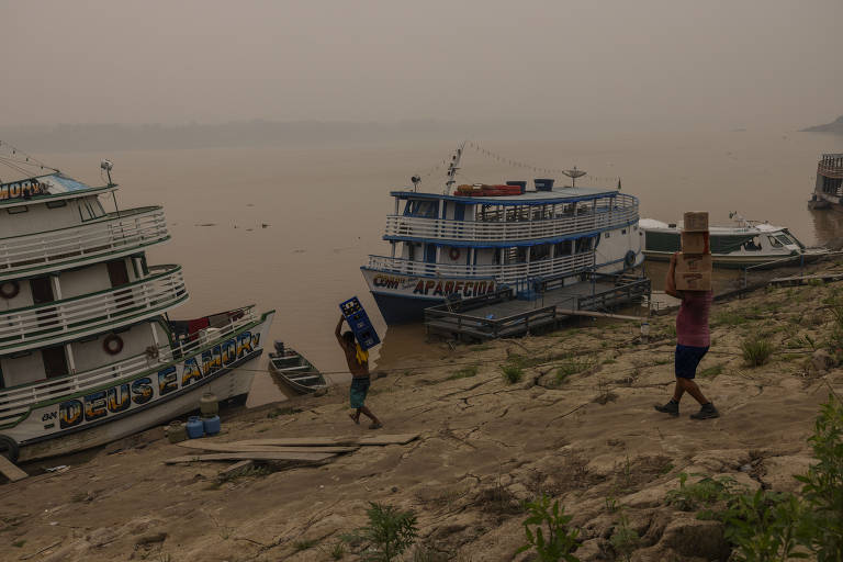 Homem carrega barco com mercadoria às margens do rio Madeira em Porto Velho, em meio a fumaça das queimadas que há dias cobre a capital de Rondônia
