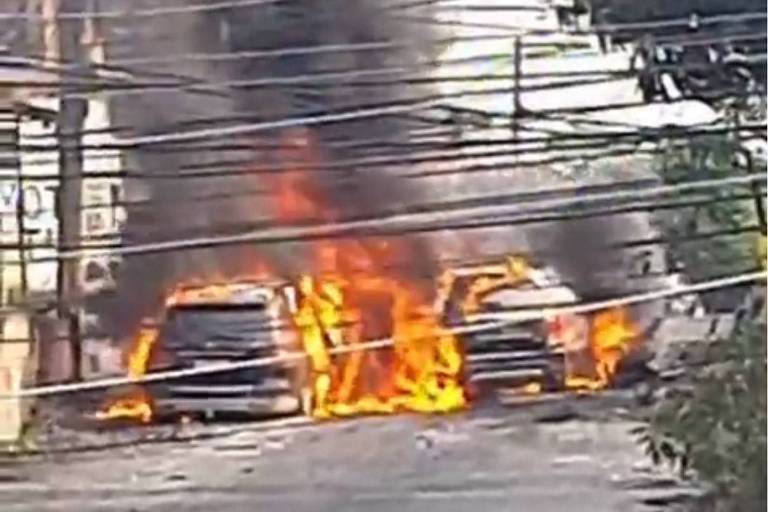 Imagem colorida mostra dois carros incendiados e utilizados como barricadas no meio de uma rua no Complexo do Salgueiro, em São Gonçalo, na Região Metropolitana do Rio