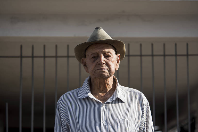 Homem idoso de camisa branca com listas finas azuis e com chapéu