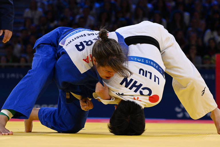 Brenda Freitas, do Brasil, com quimono azul, tenta aplicar golpe em Li Liu, da China, de quimono branco e com a cabeça encostada no chão