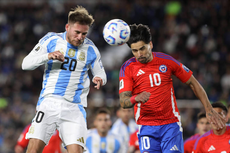 A imagem mostra dois jogadores de futebol em ação durante um jogo entre Argentina e Chile. O jogador da Argentina, vestindo uma camisa listrada em azul e branco com o número 20, está tentando cabecear a bola, enquanto o jogador chileno, usando uma camisa vermelha com o número 10, também se prepara para a disputa. O fundo apresenta uma multidão de torcedores, indicando que o jogo está acontecendo em um estádio.
