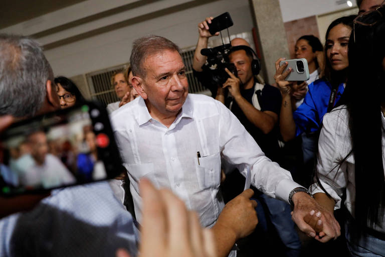 Edmundo González, homem branco, idade avançada, está de camisa branca e dá a mão a uma pessoa que não aparece na foto. Ele caminha, enquanto algumas pessoas o fotografam. 