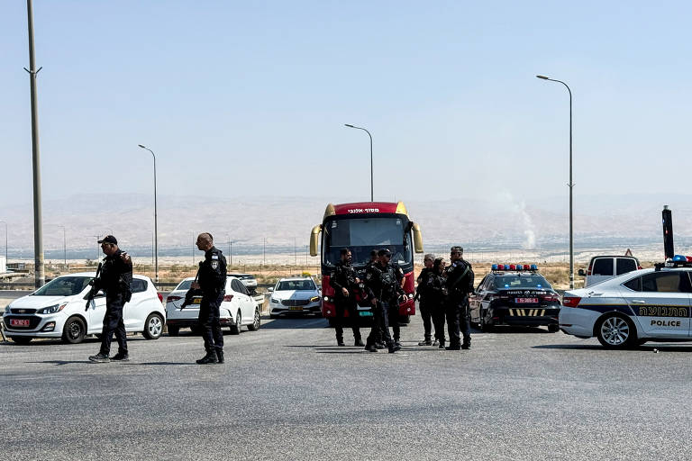 Um grupo de policiais anda por uma estrada em frente a quatro carros, um ônibus e uma van.