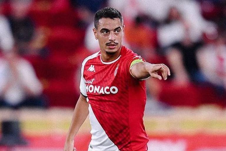 Em foto colorida, jogador com uniforme vermelho e branco aparece dando instruções no gramado