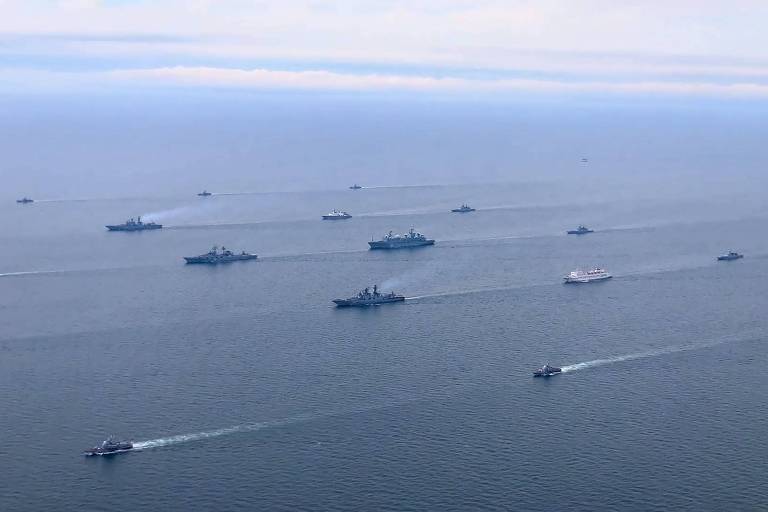 Foto aérea mostra grande área de oceano com diversos navios de guerra cinzentos em manobra. O céu está parcialmente nublado 