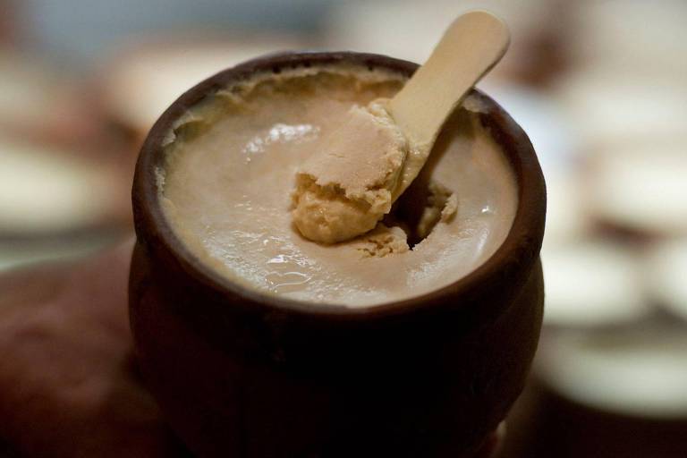 Uma pequena pazinha de madeira mergulhada em uma panela de barro com kulfi, sobremesa gelada indiana
