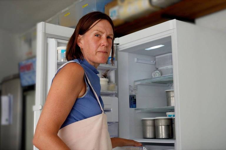 Mulher branca de cabelo curto em frente a um freezer aberto
