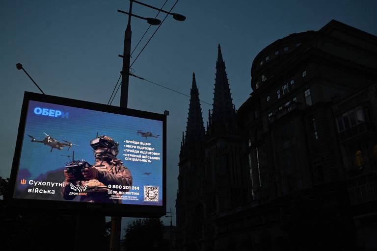 Foto mostra um outdoor com a imagem de um soldado operando drones ainda ligado, enquanto os edifícios em volta estão no escuro, assim como o céu, durante blecaute em Kiev