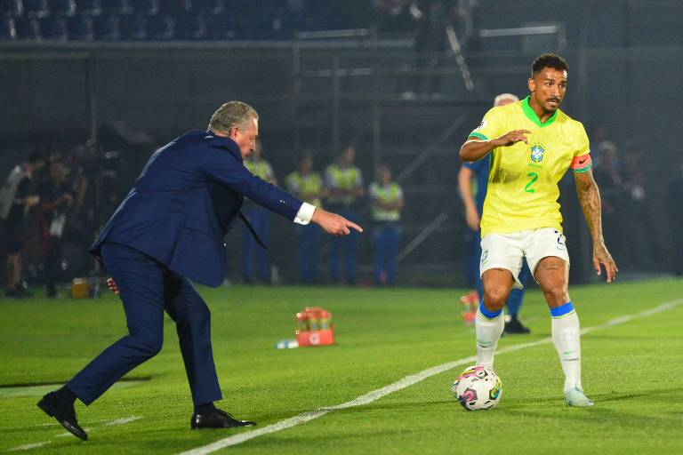 Observado pelo treinador Gustavo Alfaro, do Paraguai, o lateral e capitão Danilo, da seleção brasileira, que usa camisa amarela, conduz a bola em partida em Assunção pelas Eliminatórias da Copa do Mundo de 2026