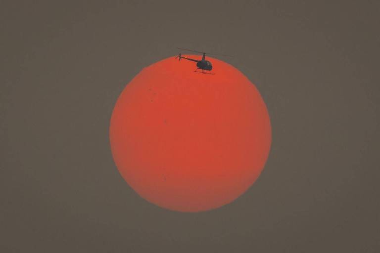 Um helicóptero voa através do sol alaranjado pela fumaça dos incêndios em São Paulo
