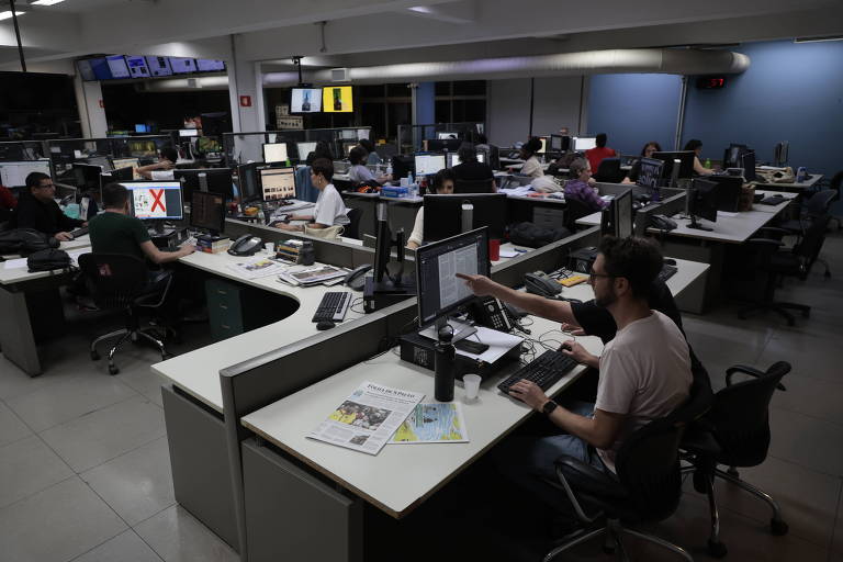 Foto mostra a Redação da Folha, um ambiente de escritório com diversas mesas, cadeiras e computadores; o ambiente está repleto de jornalistas e diagramadores trabalhando no fechamento da primeira edição da Folha no formato berliner