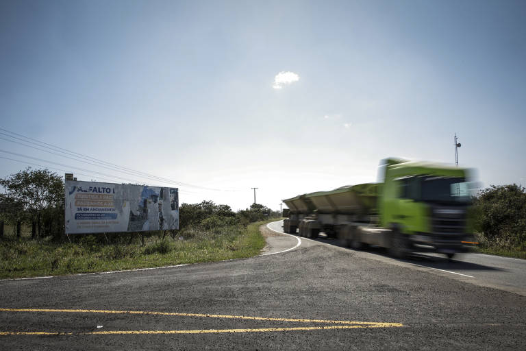 Estrada com outdoor na margem. Um caminhão verde passa em velocidade