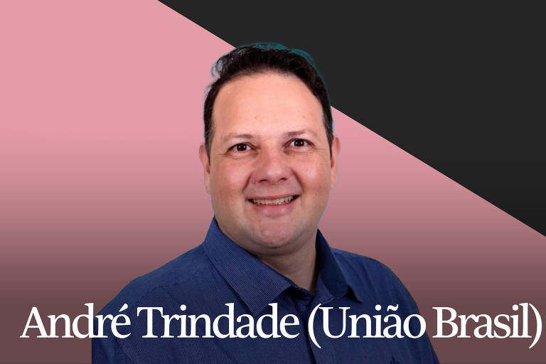 André Trindade, homem branco de cabelos escuros, olha para a câmera e sorri, marcando as bochechas