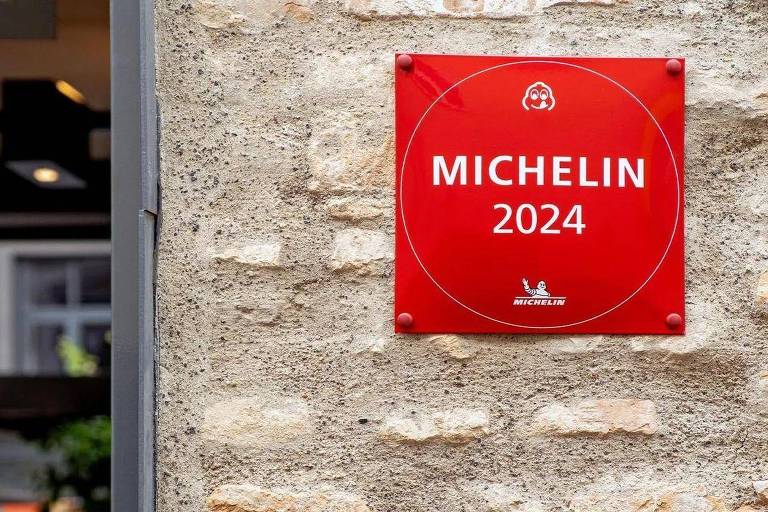 Uma placa vermelha com o logotipo da Michelin e a inscrição 'MICHELIN 2024' fixada em uma parede de pedra. A placa é circular e destaca a distinção do guia Michelin para o ano de 2024.