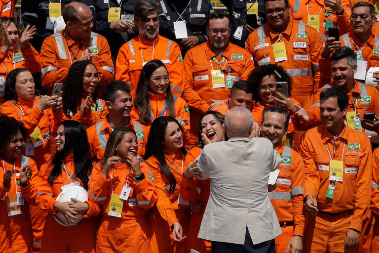 Homem de terno claro, de costas, cumprimenta dezenas de pessoas vestidas com univorme laranja vivo