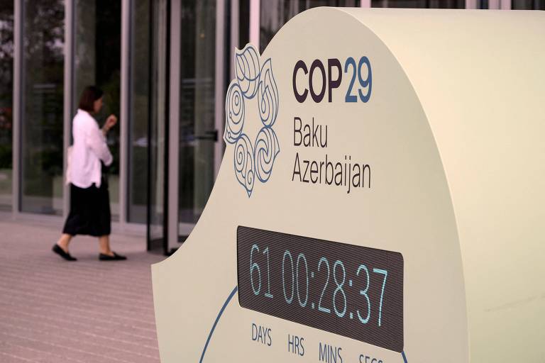 Contador com logo da COP29; uma mulher caminha ao fundo em uma calçada