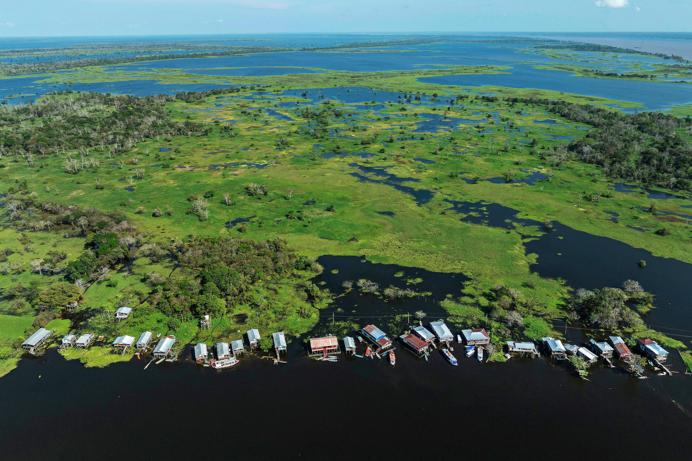 Vista de drone de lago com água escura e muitos barcos próximos a uma margem com vegetação preservada