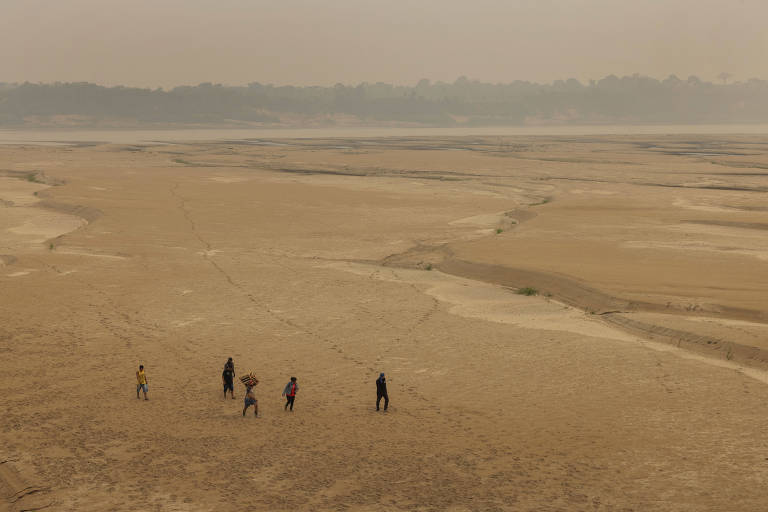 Vista de drone de cinco pessoas que caminham na areia; há muita fumaça no céu