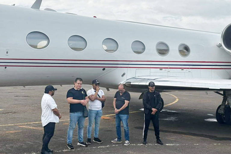 Na foto há cinco homens em frente a um avião 