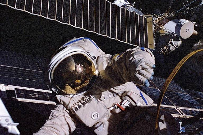 Um astronauta trabalhando no espaço, segurando uma nave espacial.
