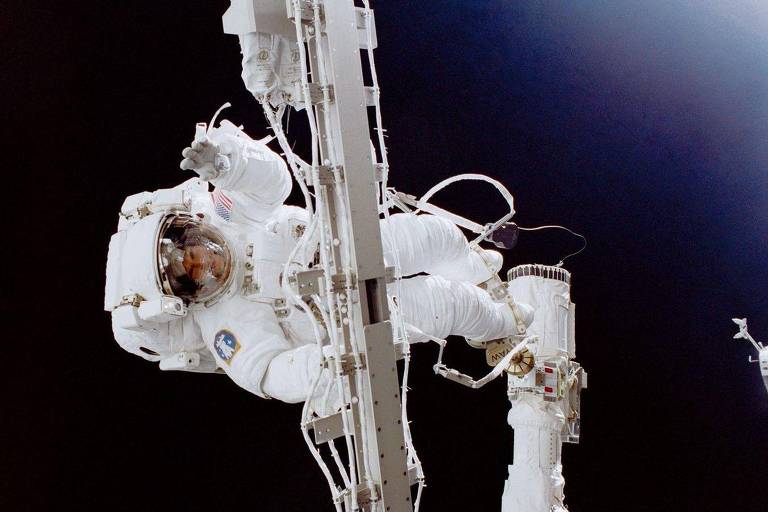 Um astronauta trabalhando no espaço, segurando uma nave espacial
