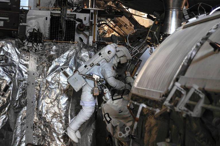 Um astronauta segurando uma nave espacial enquanto realiza manutenção.
