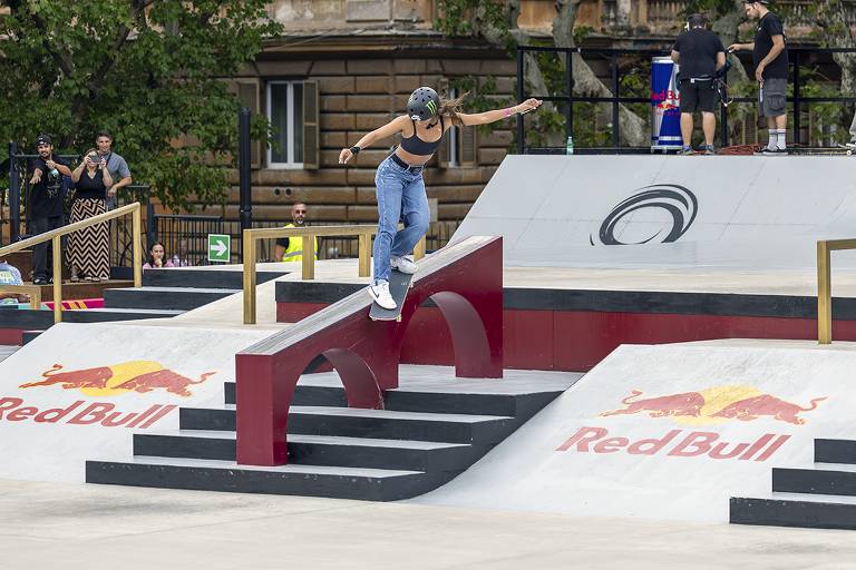 Rayssa Leal desce uma rampa com o skate. Ela usa calça jeans, um top preto e capacete