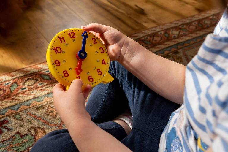 Mão de criança segurando relógio de brinquedo.
