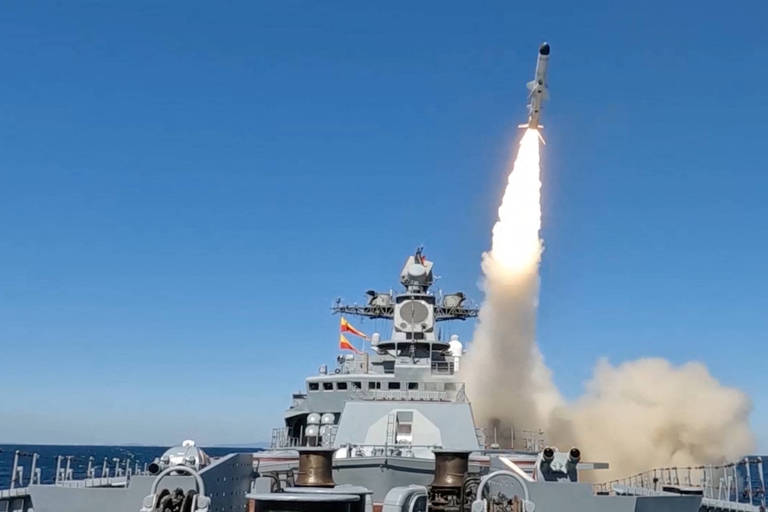 Em um dia de céu azul, míssil é disparado de um navio de guerra cinzento, deixando para trás uma trilha de fogo e fumaça