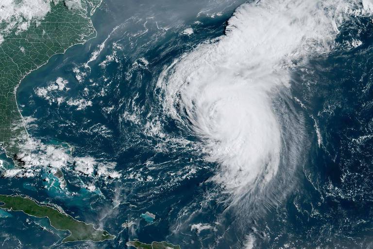 Imagem de satélite mostrando um furacão no Oceano Atlântico, com nuvens espessas e um padrão de rotação visível. A costa leste dos Estados Unidos e as ilhas do Caribe estão visíveis ao fundo.
