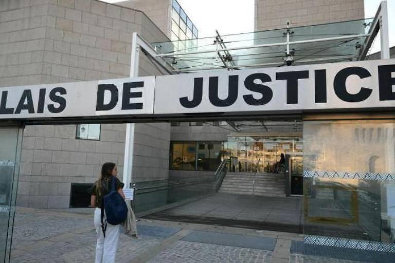 A imagem mostra a entrada do Palais de Justice, com uma grande placa na parte superior que diz 'PALAIS DE JUSTICE' em letras maiúsculas e em negrito. À esquerda, uma mulher com uma mochila está se aproximando da entrada, que é composta por uma estrutura de vidro e metal. Ao fundo, é possível ver escadas que levam para dentro do edifício.