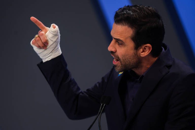 Foto mostra Pablo Marçal, homem branco de cabelo preto, barba por fazer e camisa escura, gesticula com o dedo em riste. Sua mão e antebraço estão enfaixados. 