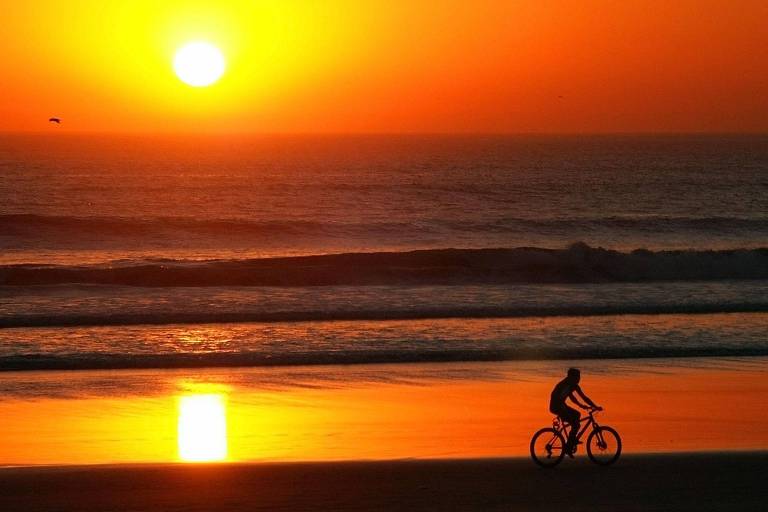 Pessoa andando de bicicleta à beira do mar ao pôr do sol
