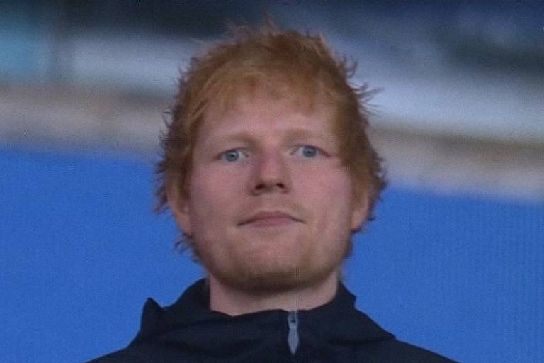 Ed Sheeran, homem ruivo, olha para frente com semblante sério