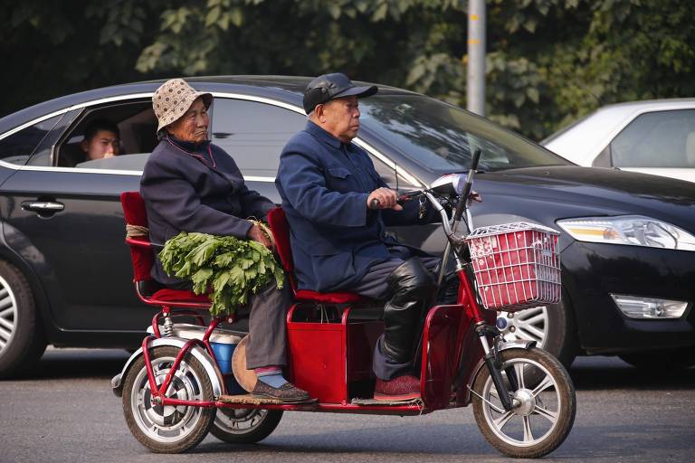 Casal de idosos em triciclo, transportando verduras ao longo de uma rua, em Pequim, na China