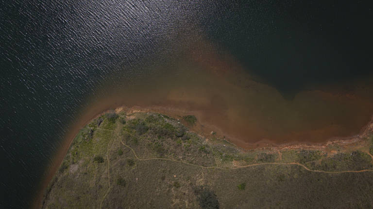 Imagem aérea de um pequeno pedaço de terra cercado pela água da represa, com vegetação seca.