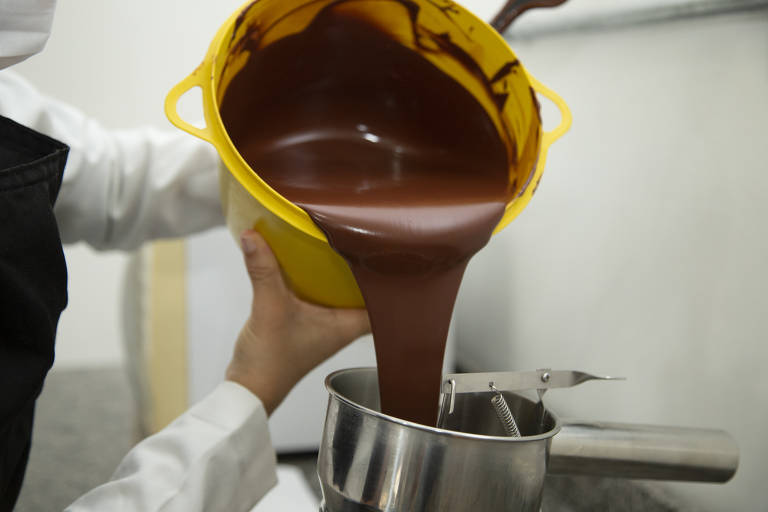 Foto mostra chocolate antes de virar barras em linha de produção na Bahia; produto é despejado de um balde amarelo