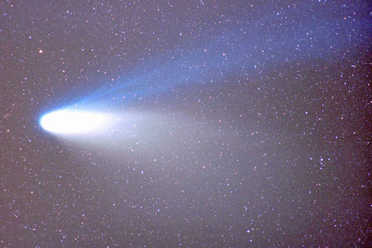 A imagem mostra um cometa com uma cauda brilhante e azulada, se movendo através de um céu repleto de estrelas. A parte frontal do cometa é iluminada, enquanto a cauda se estende em direção ao fundo escuro do espaço.