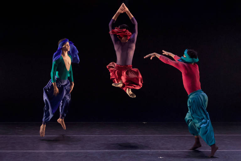 Três bailarinos dançam, o do meio está pulando