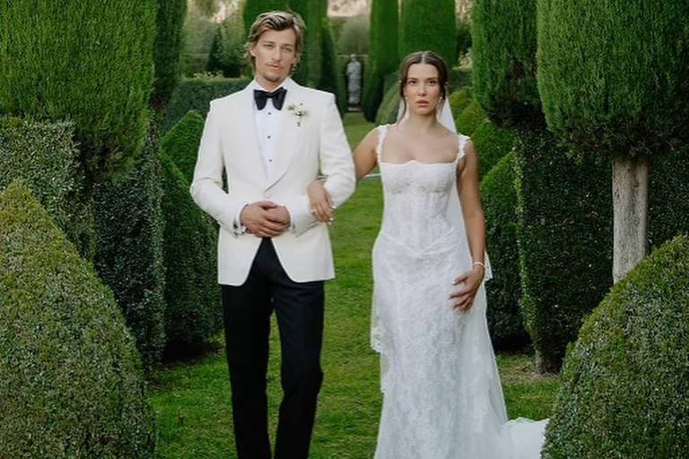 Um casal posando em um jardim bem cuidado, cercado por altas árvores em forma de cone