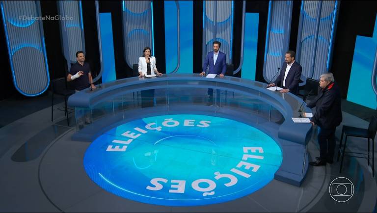 Foto de cima do palco do debate da Globo em São Paulo, os candidatos estão organizados atrás de uma mesa em semicírculo, com um círculo iluminado no chão