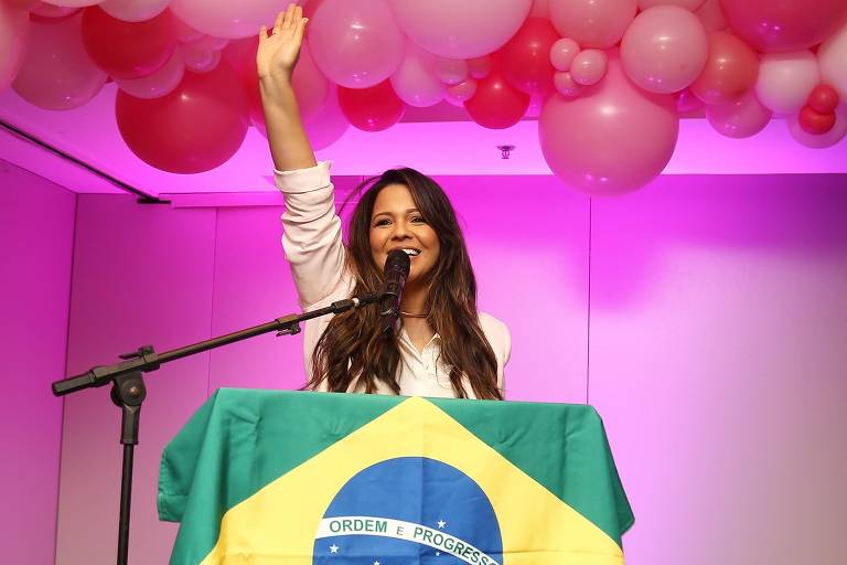 Mulher com braços levantados em frente a bandeira do Brasil