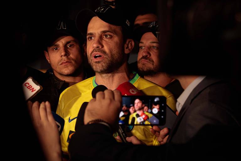 homem de boné com a letra M e camiseta da seleção brasileira de futebol fala diante de microfone