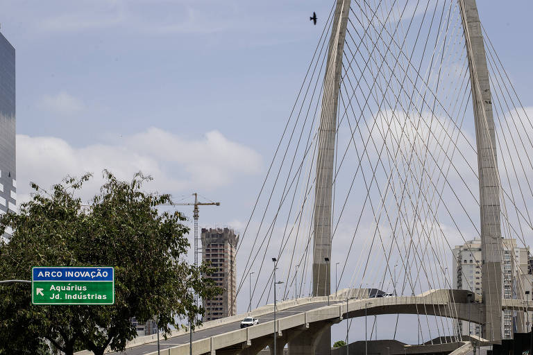 Vista de uma ponte estaiada. Ao fundo, céu azul com nuvens