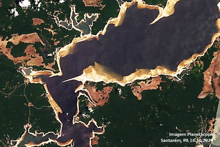 A imagem mostra uma vista aérea de um rio cercado por áreas verdes e algumas formações de terra. O lago apresenta uma coloração escura, enquanto as margens são delineadas por uma faixa clara. Há também áreas de vegetação densa ao redor do lago, com algumas partes expostas. A imagem é uma captura de satélite