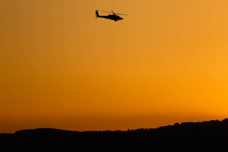 A imagem mostra um helicóptero em silhueta voando contra um fundo amarelo vibrante, que representa um pôr do sol. Abaixo do helicóptero, há uma linha de montanhas escuras, criando um contraste com o céu iluminado.